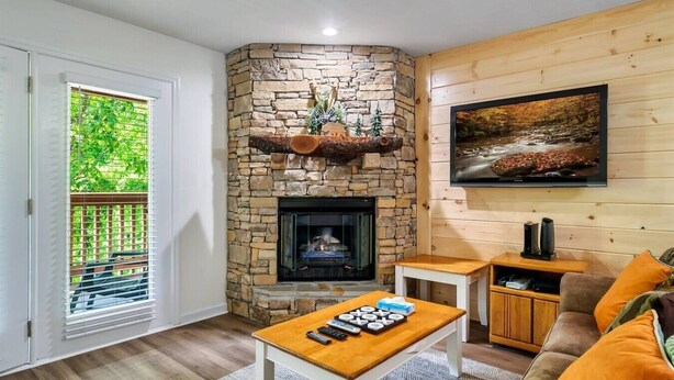 A living room with a stone fireplace, a television mounted on the wall, and a view of greenery through a window. - 1 Mile to Dollywood and Pigeon Forge Strip! (Pigeon Forge)