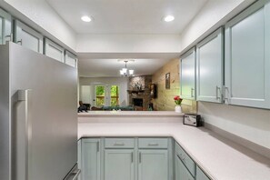 A kitchen with light-colored cabinets, a stone fireplace, and a view into a dining area.