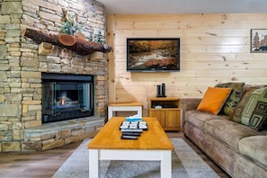 Un salon chaleureux avec une cheminée en pierre, un téléviseur à écran plat, une table basse en bois et un canapé confortable.