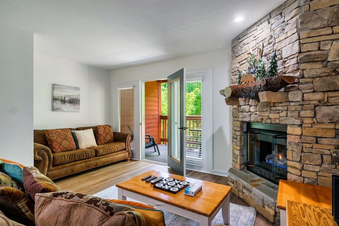Uma sala de estar com lareira de pedra, um sofá, uma mesa de centro com controles remotos e uma porta que dá para um pátio externo.