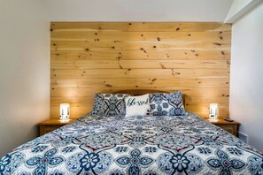 Ein Bett mit einem gemusterten Überwurf, zwei Nachttischlampen und einem Holz-Kopfteil.