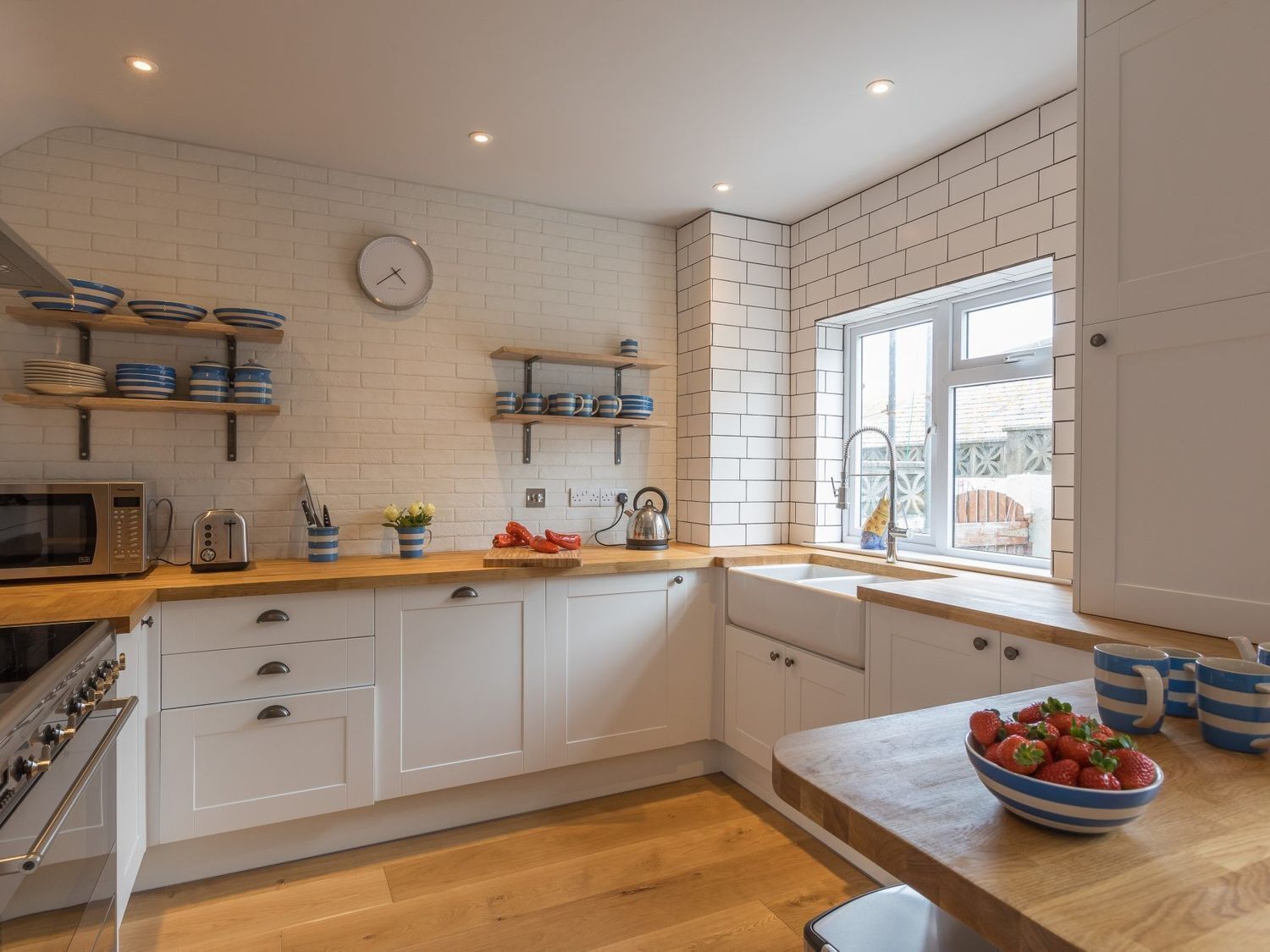 A modern kitchen with white cabinetry, wooden countertops, and a large window providing natural light.