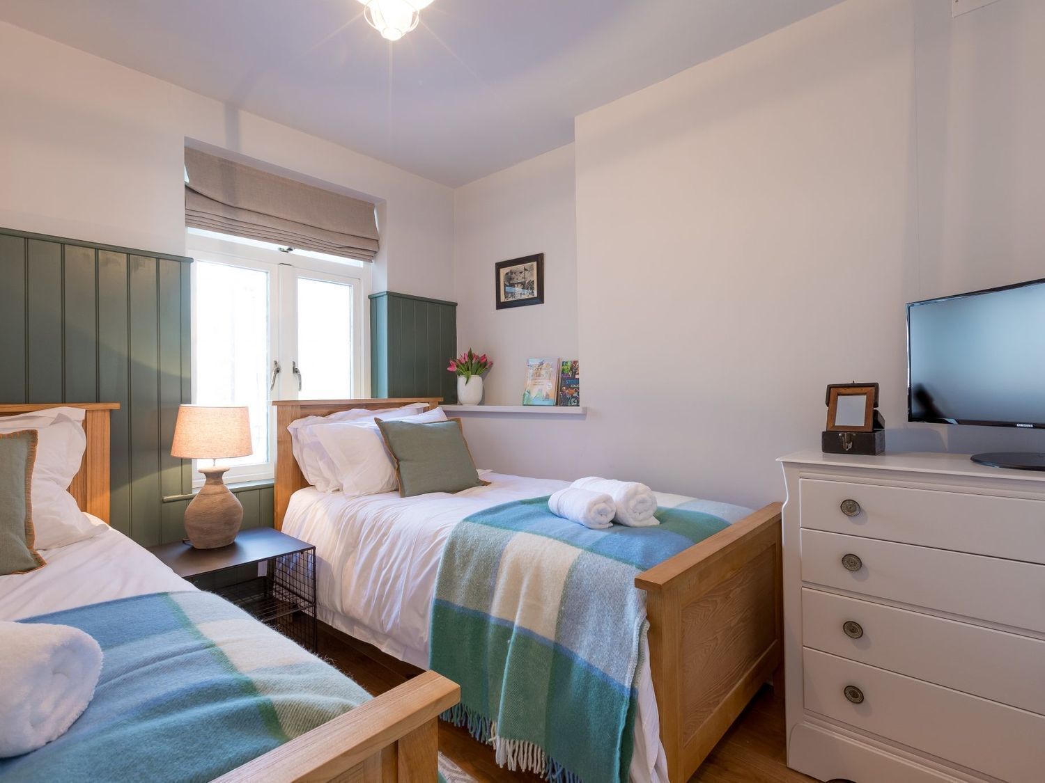 Une chambre avec deux lits, une télévision, une commode et une fenêtre avec des rideaux.
