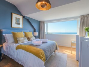 A modern bedroom with a large bed, a view of the sea, and a framed picture on the wall. - Marchbourne (St Ives)