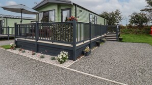 A green mobile home with a deck, surrounded by gravel and small plants. - Jean's Place (Malton)