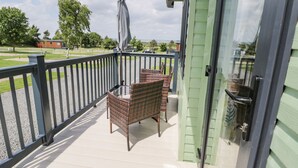 A balcony with wicker furniture and a grill, overlooking a green lawn and trees. - Jean's Place (Malton)