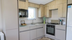 A modern kitchen with wooden cabinets, a built-in microwave, a gas stove, and a stainless steel sink. - Jean's Place (Malton)