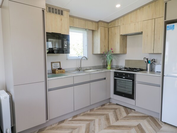 A modern kitchen with wooden cabinets, a built-in microwave, a gas stove, and a stainless steel sink.
