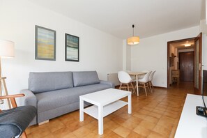 Un salon comprenant un canapé, une table basse blanche, une table à manger avec des chaises et un luminaire suspendu.