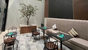 A modern interior with a high ceiling, a seating area with a sofa and chairs, a small table, and a decorative tree. - VOYAGE RESIDENCE (Riyadh)