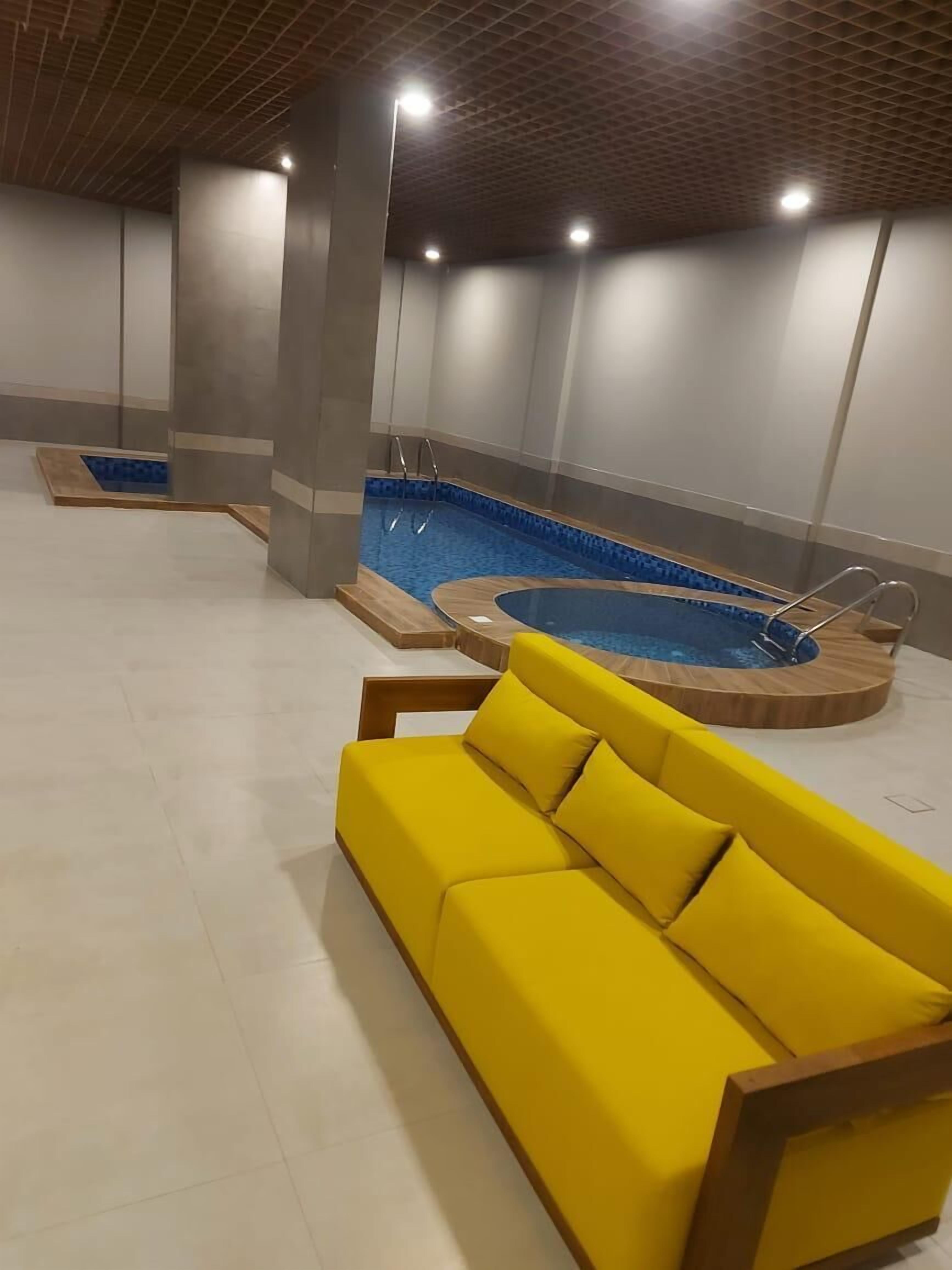 A modern indoor pool area with a yellow sofa and two hot tubs.