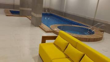 A modern indoor pool area with a yellow sofa and two hot tubs.