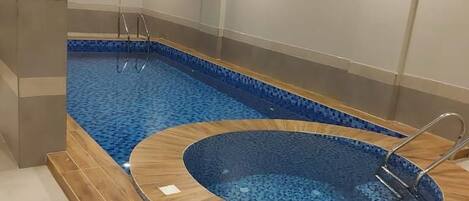 A swimming pool with a wooden deck and a hot tub.