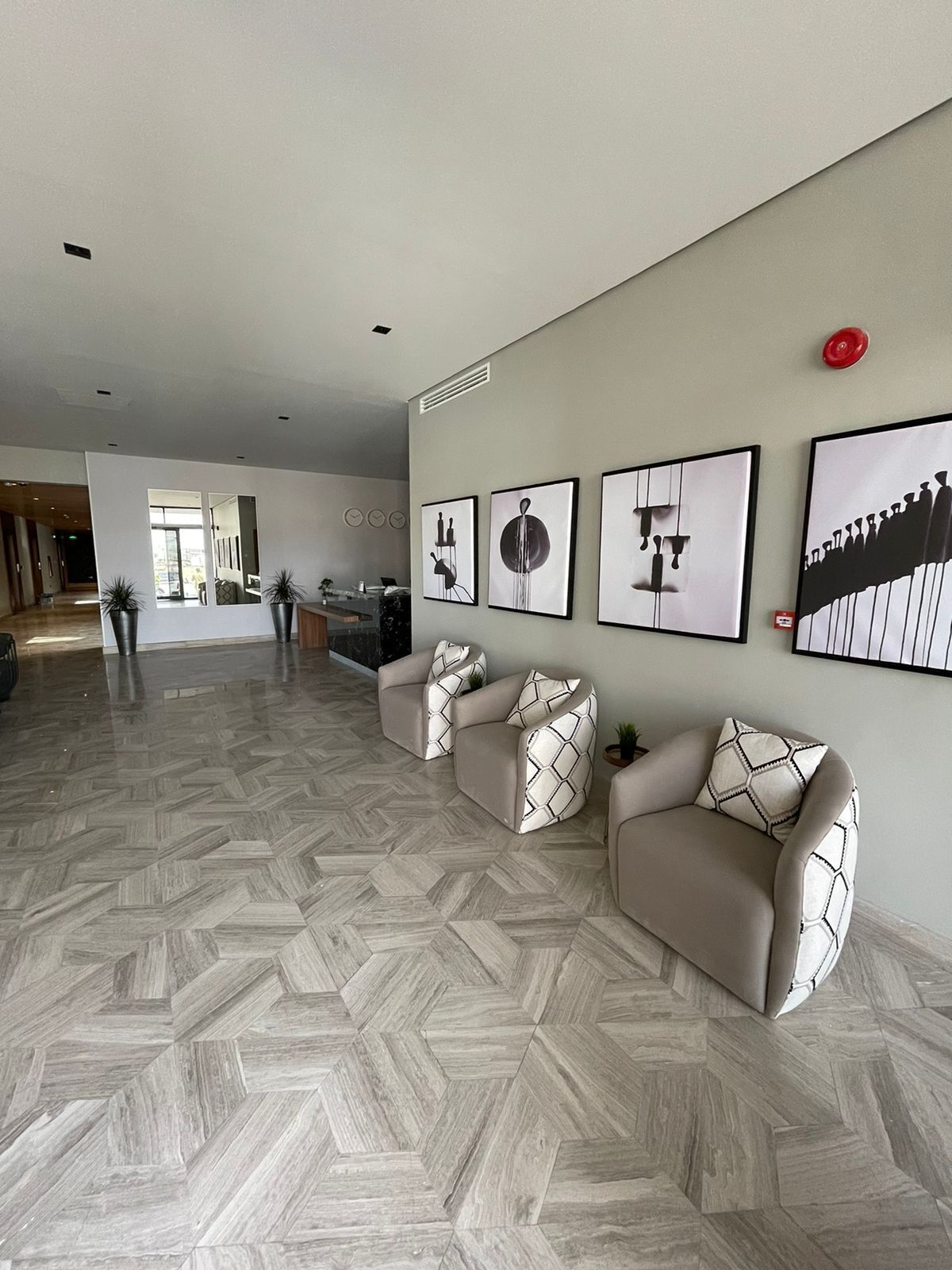 A spacious living area with a herringbone floor pattern, a sofa set, and a wall with framed artwork.