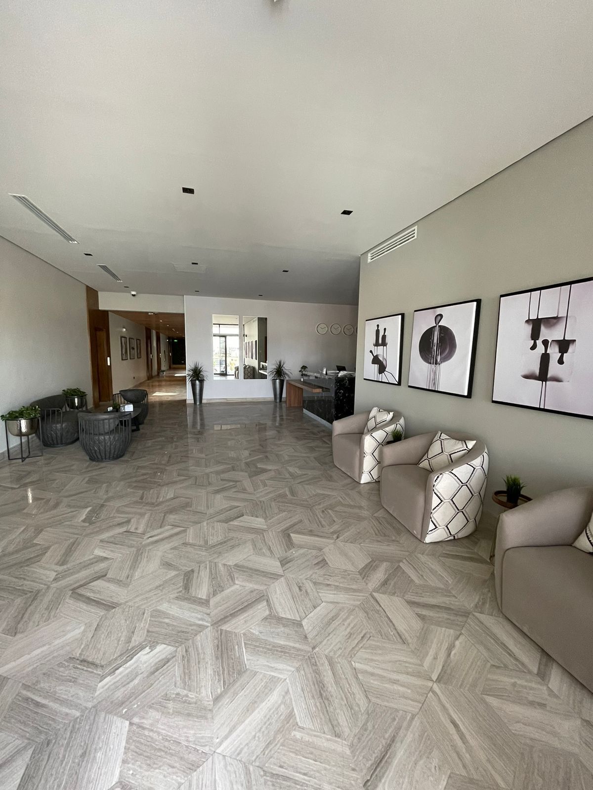 A spacious living area with a herringbone floor pattern, a sofa set, and several wall-mounted artworks.