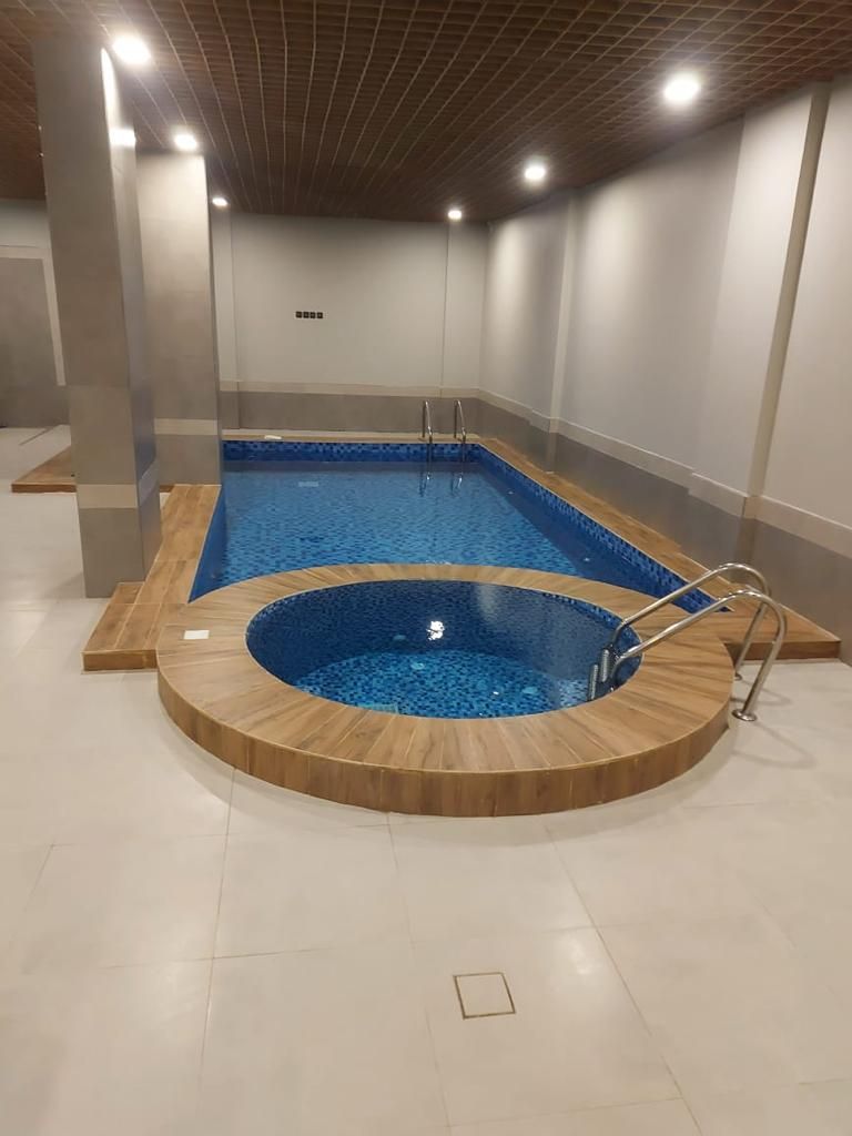 A swimming pool with a wooden deck and a circular hot tub.