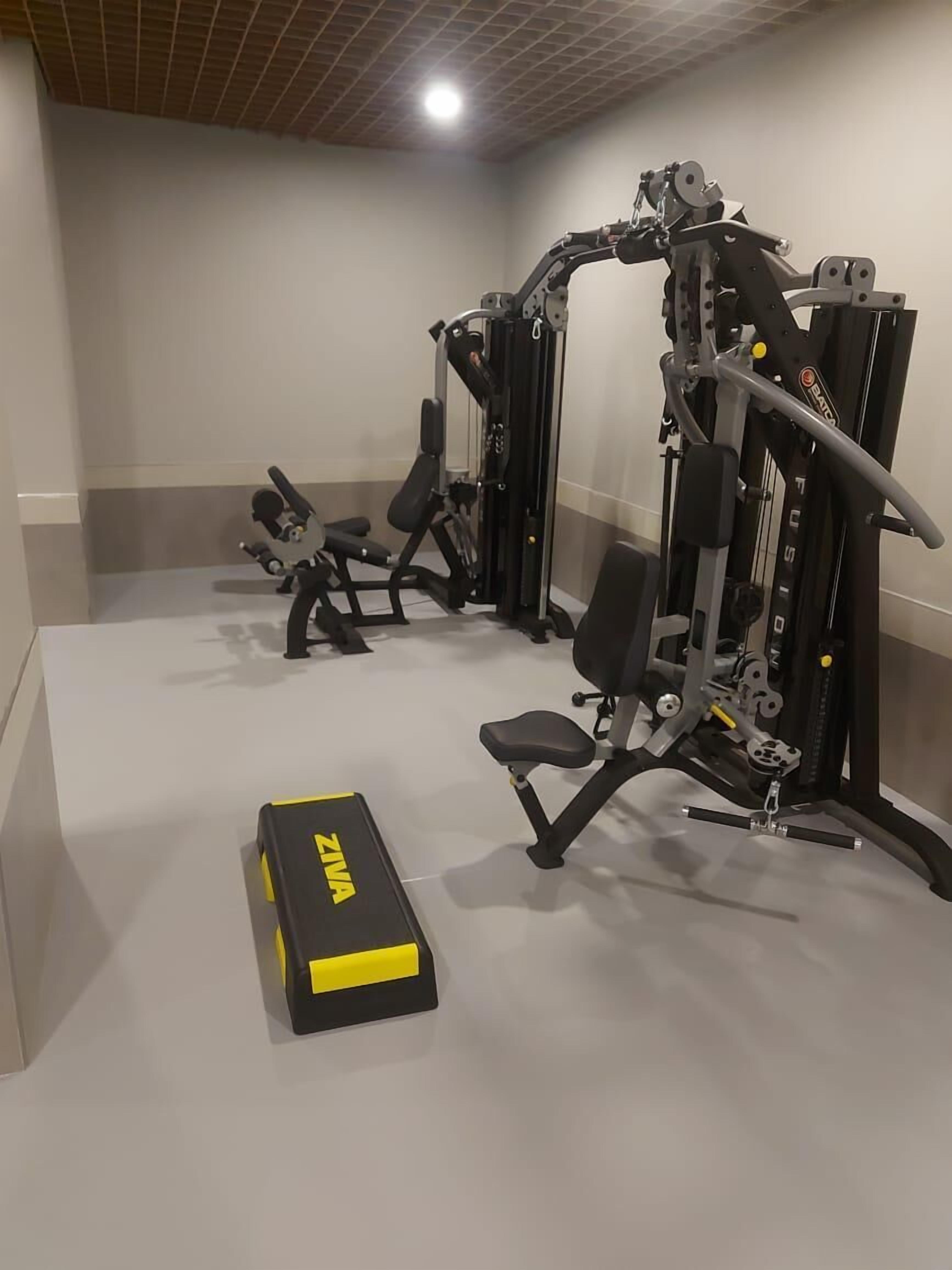 Un gimnasio con equipamiento de levantamiento de pesas, una banca y una jaula para sentadillas.