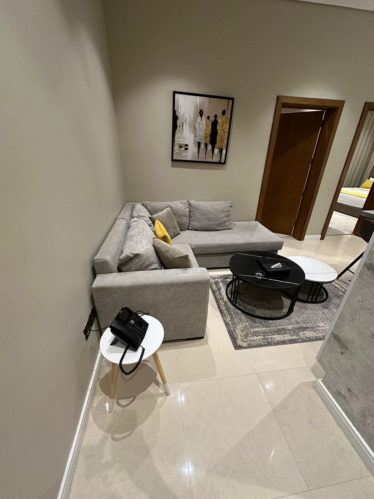 A modern living room with a grey sectional sofa, a small white side table, a black coffee table, and a framed artwork on the wall.