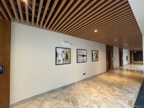 A hallway with wooden slatted ceiling, framed artwork on the walls, and a patterned floor. - VOYAGE RESIDENCE (Riyadh)