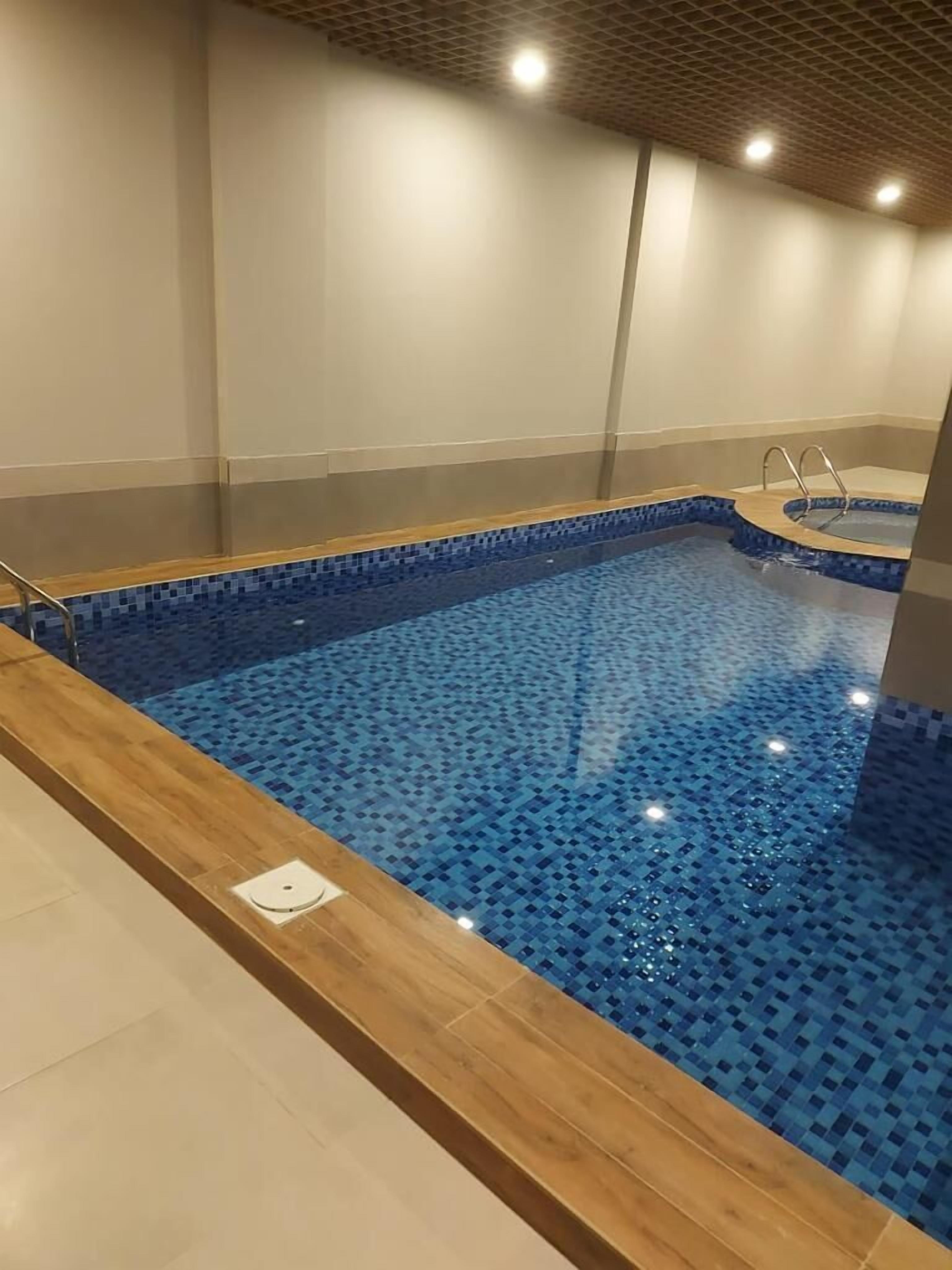 A swimming pool with a tiled floor and a wooden deck surrounding it.
