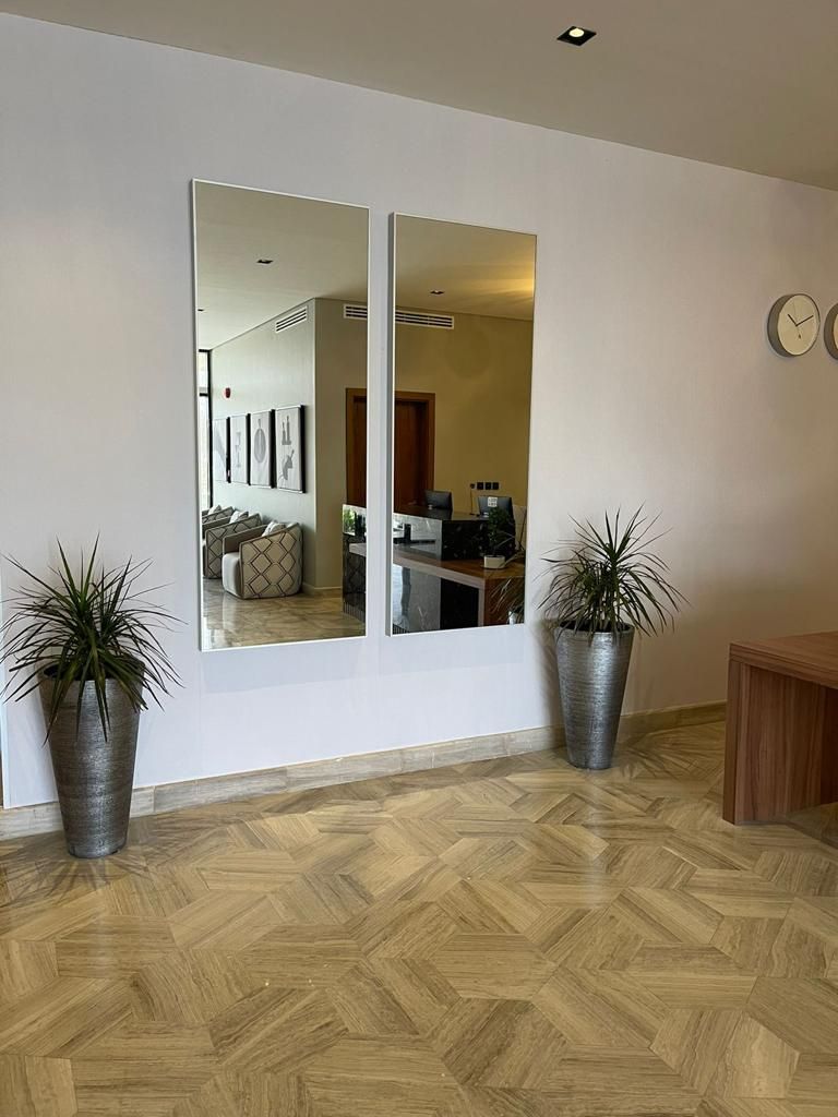 Quarto com um espelho grande, duas plantas em vasos, um banco de madeira e piso com padrão herringbone.