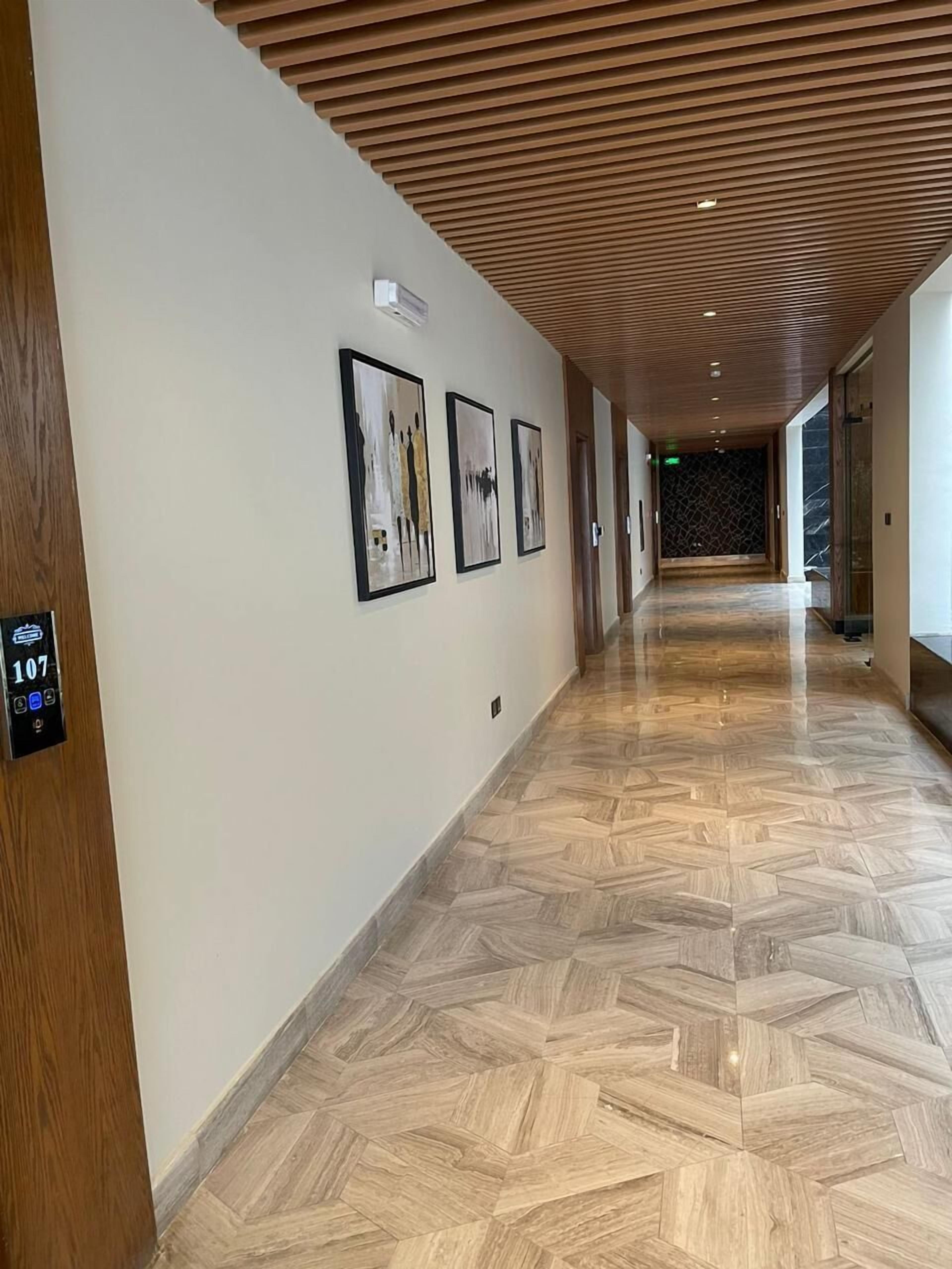 A hallway with a wooden ceiling, a herringbone floor pattern, and three framed artworks on the wall.