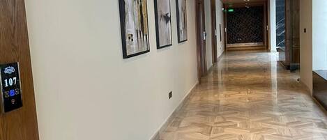 A hallway with a wooden ceiling, a herringbone floor pattern, and three framed artworks on the wall.