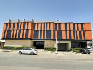A modern building with a flat roof, large windows, and a parking lot with cars. - VOYAGE RESIDENCE (Riyadh)