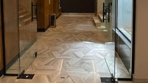 A modern hallway with glass doors, wooden paneling, and patterned flooring. - VOYAGE RESIDENCE (Riyadh)