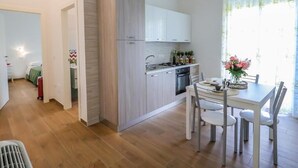 Una cuina moderna amb armaris blancs, una taula de menjador amb caires i una finestra amb cortines.