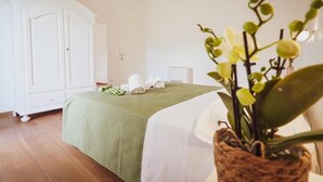 Habitació d'hotel amb un llit, un estri de llit verd, un armari blanc i una orquídia en test.