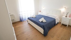 Un dormitori amb llit, taules de nit, un radiador i una finestra amb cortines.