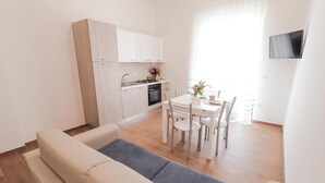 Una cuina moderna amb armaris blancs, una taula de dinar amb cadires i un televisor de pantalla plana muntat a la paret.