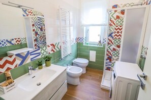 A bathroom with a sink, bidet, and toilet, tiled with geometric patterns. - Double bed and sofa bed (Laureana Cilento)