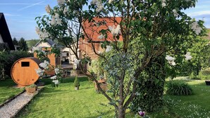 Un jardín con un árbol, un barril de madera y una casa de techo rojo.