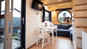 Una habitación acogedora con interior de madera, un espejo redondo, un televisor en la pared, una mesa de comedor con sillas y un sofá.