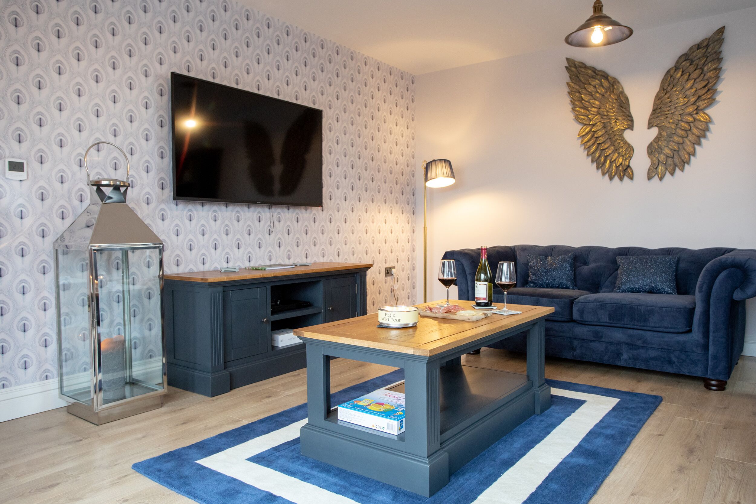 Ein modernes Wohnzimmer mit Flachbildfernseher, einem dekorativen Flügelspiegel, einem Holztisch und einem blauen Sofa.