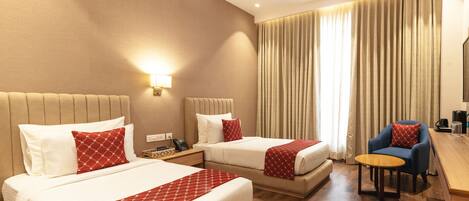 A hotel room with two beds, a desk, a chair, a lamp, and a large window with curtains.