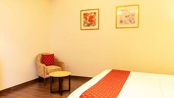 Quarto de hotel com uma cama, uma mesa redonda pequena, uma cadeira e duas obras de arte emolduradas na parede.