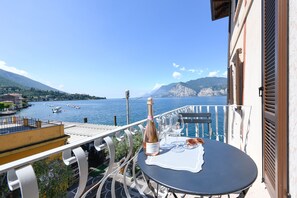 A balcony with a table set for two, overlooking a coastal view with boats and mountains. - Appartamento del Marinaio (Malcesine)