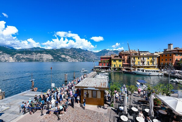 A waterfront hotel with a stone-paved dock, outdoor seating, and boats in the background. - Appartamento del Marinaio (Malcesine)