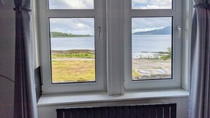 Ventana con vista a un lago, zona verde y montañas a lo lejos.