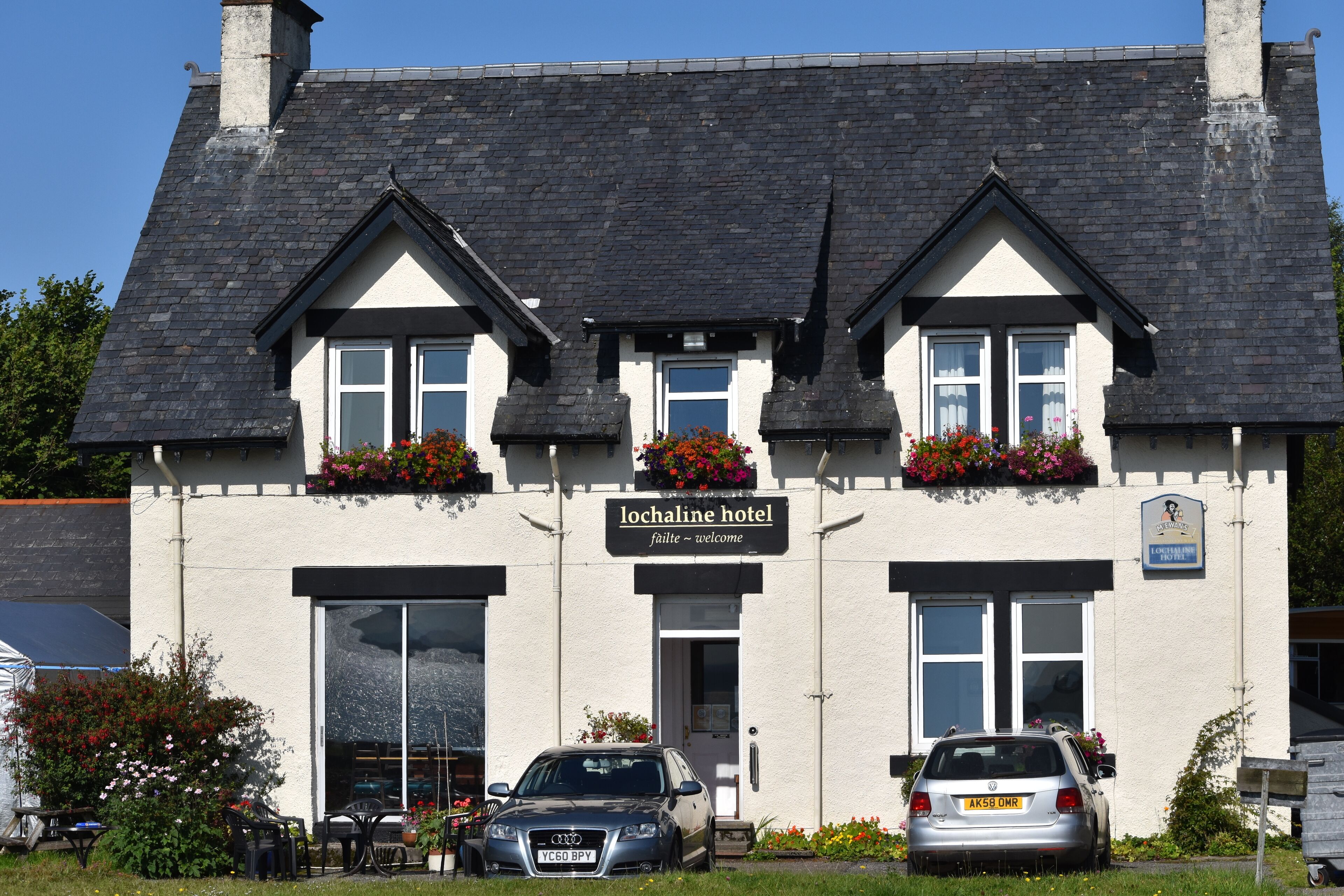 A two-story hotel with a sign reading "Lochaline Hotel." There are two cars parked in front, and the building has flower boxes on the windowsills.