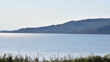 Un lago tranquilo con un velero distante, rodeado de colinas y cielos despejados.