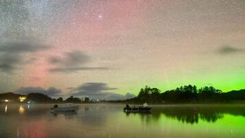 A night sky with stars and the aurora borealis over a calm lake with boats.