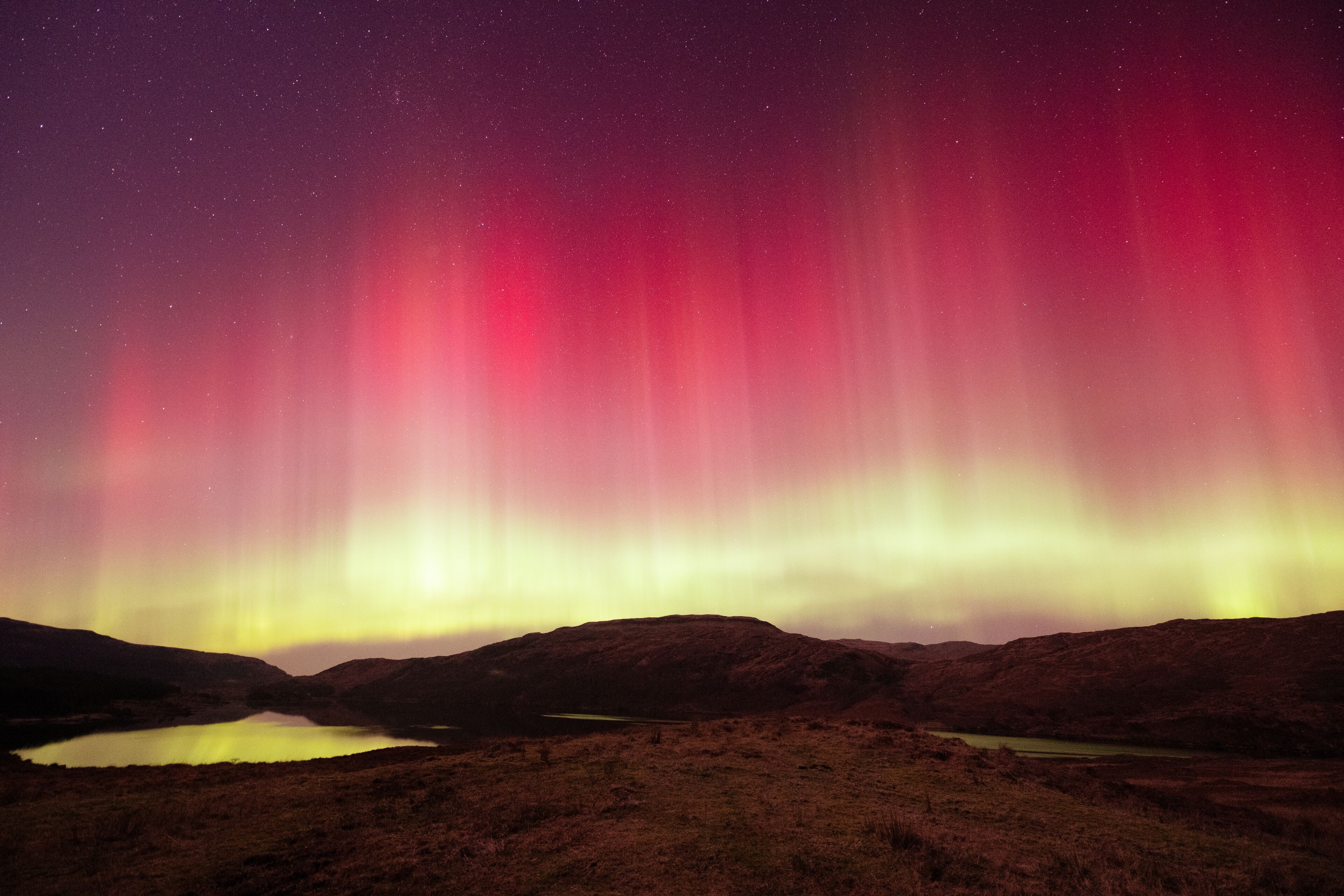 Cielo nocturno con la aurora boreal sobre un paisaje montañoso y un lago.