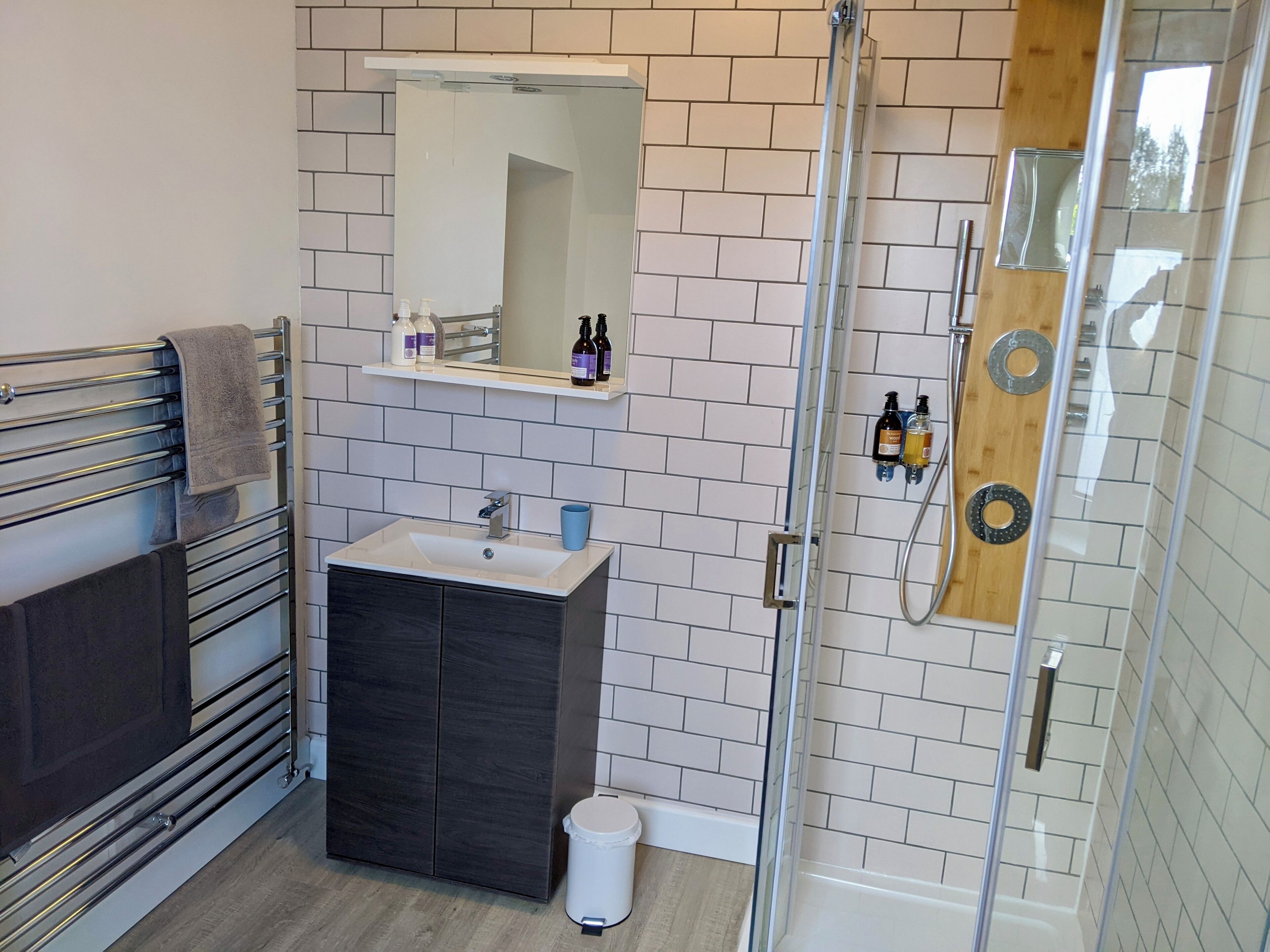 Un baño moderno con cabina de ducha de vidrio, tocador con lavamanos y espejo arriba.
