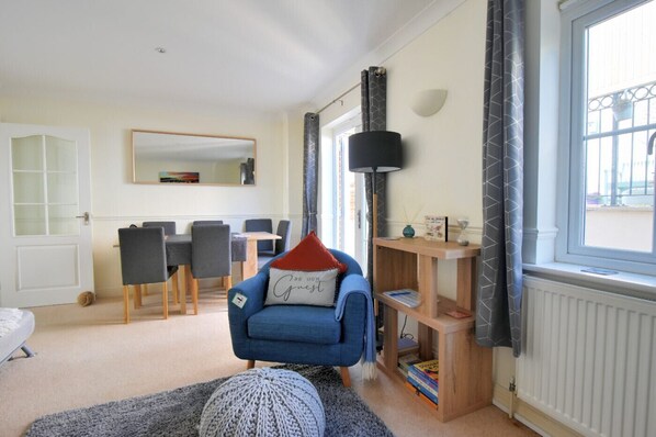 A modern living room with a blue sofa, a dining table with chairs, a large mirror, and a bookshelf.