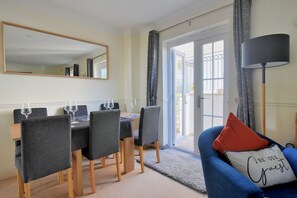 A dining area with a table set for four, chairs, a mirror, and a sofa with a cushion.