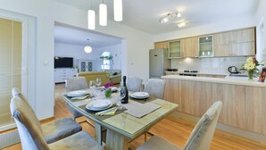Eine moderne Küche mit Kochinsel, Essbereich mit Glastisch und Wohnbereich mit Sofa und Fernseher.